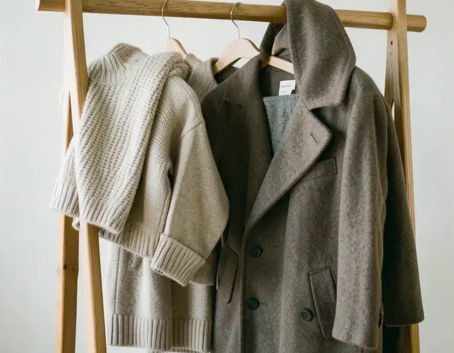 Folded knitwear and a wool coat on a wooden clothing rail