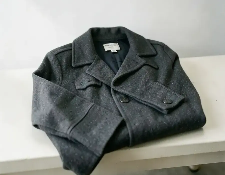Folded wool coat on a neutral bench with a size tag visible